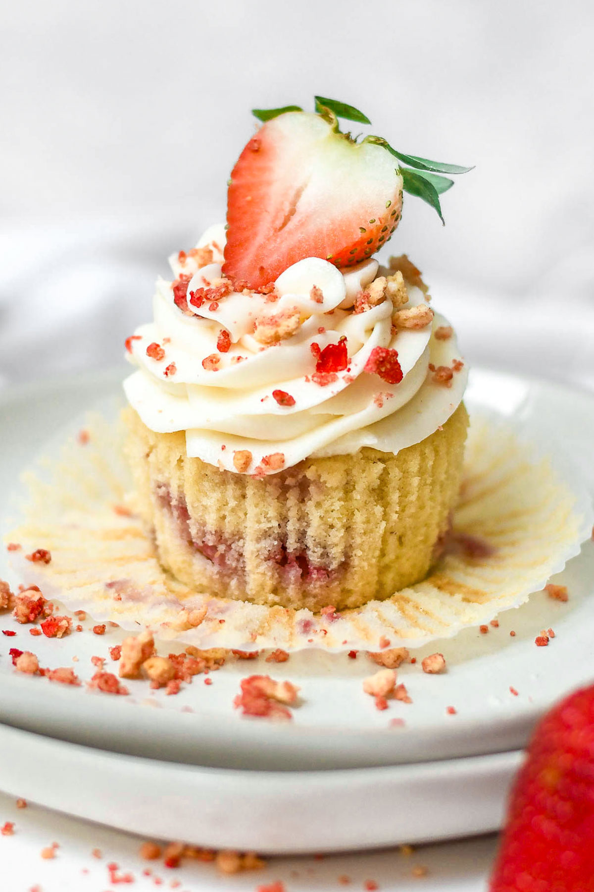 Unwrapped strawberry crunch cupcake with cream cheese frosting on top and garnished with strawberry.