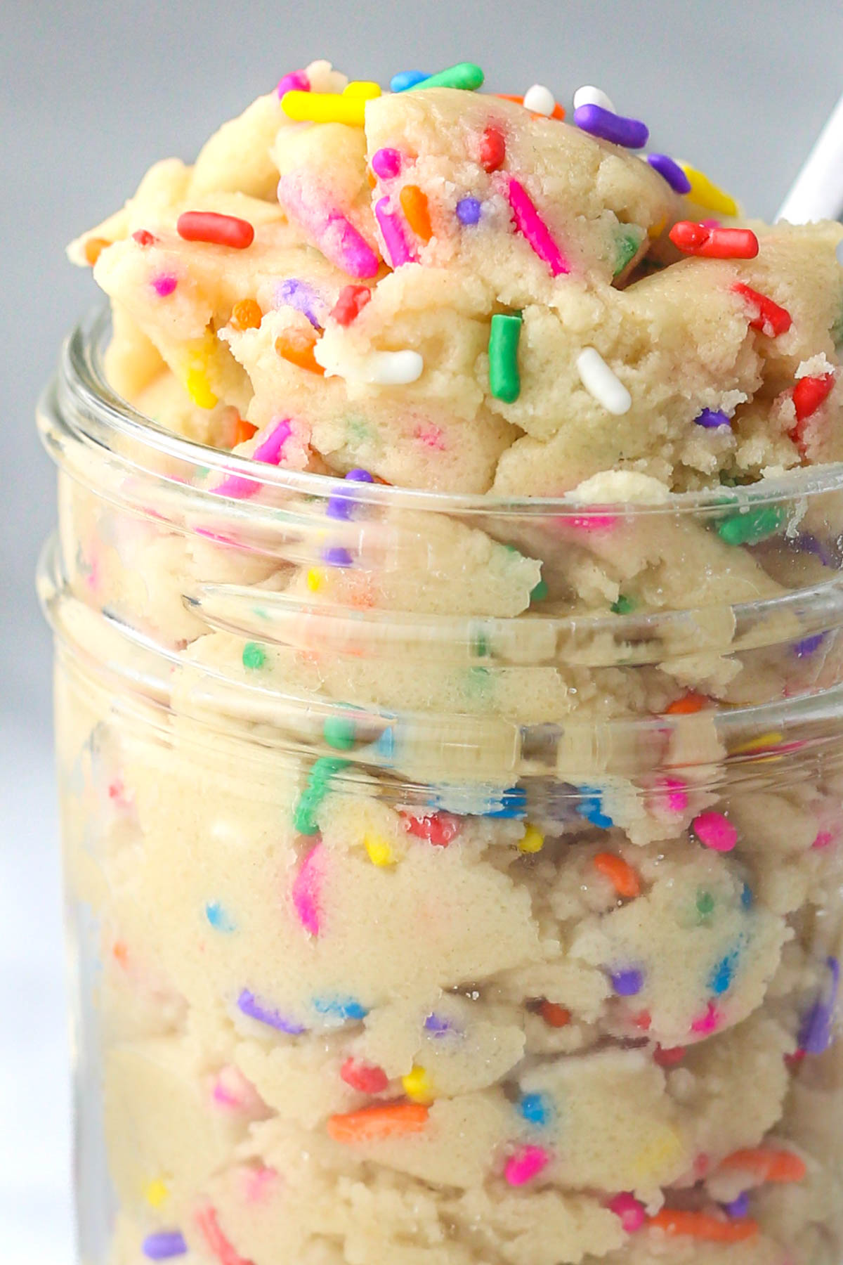 Close up of sugar cookie dough in a glass jar with rainbow sprinkles.