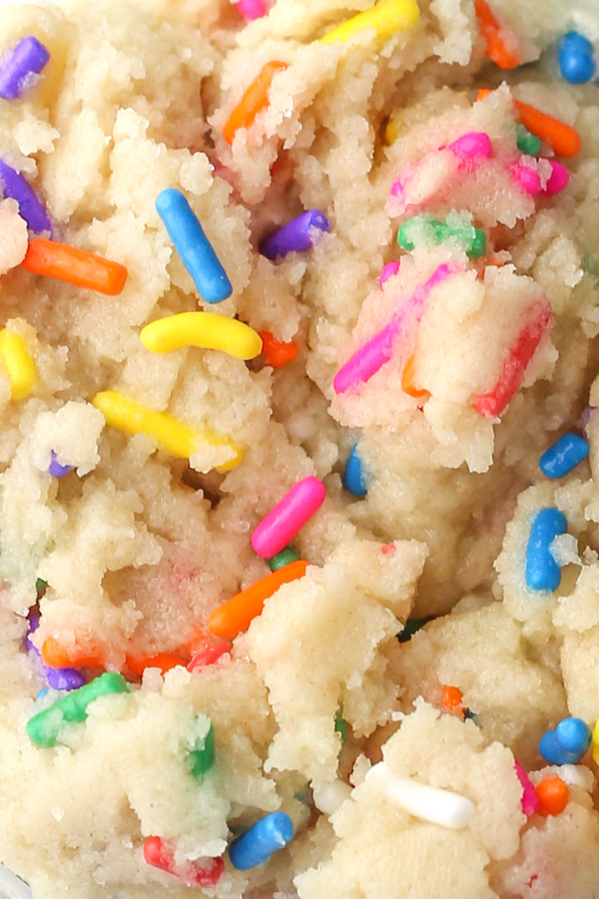 Macro shot of edible sugar cookie dough with rainbow sprinkles, showing the soft texture.
